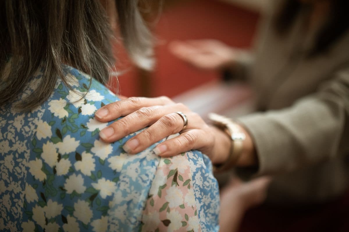 Eine Hand ruht tröstend auf der Schulter eines Menschen