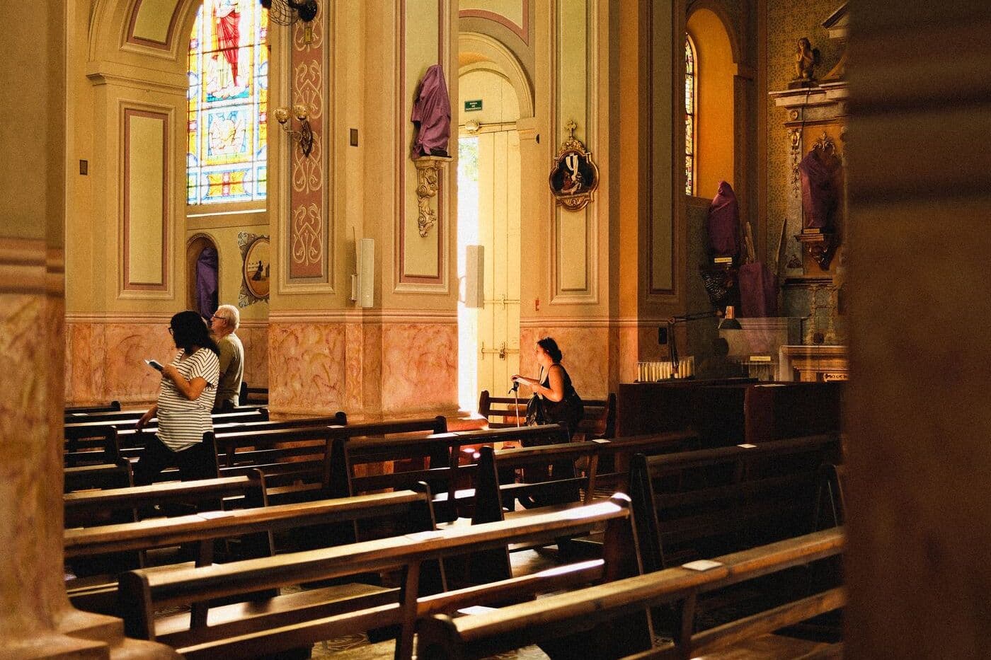Lichtdurchfluteter Innenraum einer Kirche mit Bänken und bunten Fenstern