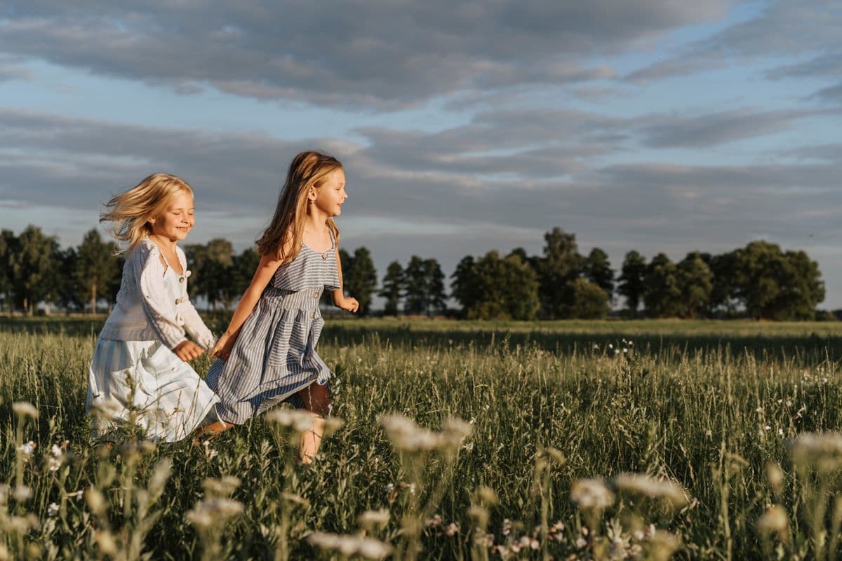 Zwei Kinder laufen fröhlich durch eine sommerliche Wiese
