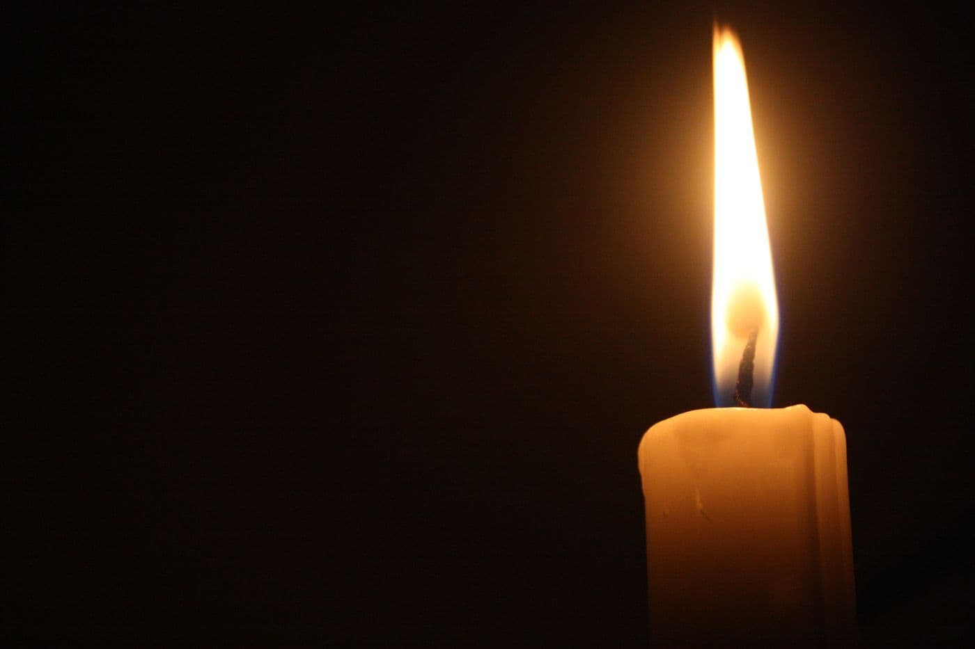 Eine brennende Kerze in warmem Licht vor dunklem Hintergrund